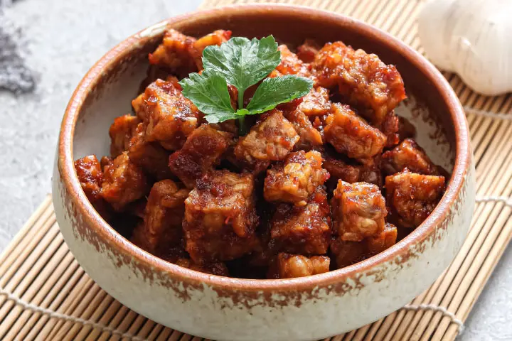 Tempeh cubes in hoisin sauce in a bowl on a table