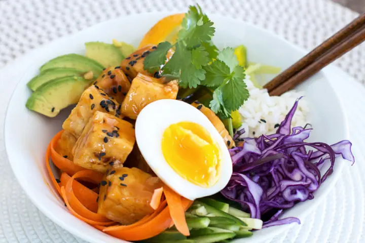 Bowl of tempeh with rice, leeks, red cabbage, carrots, avocado, cucumber and sweet‑and‑sour sauce