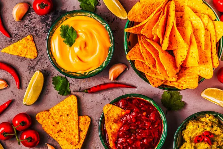 Plate of corn tortillas with cheese sauce, salsa and guacamole on a table