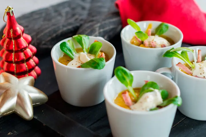 Potage à la courge Butternut et aux poireaux avec une garniture de crème fraîche, des épinards et un morceau de salami servi en portion individuelle