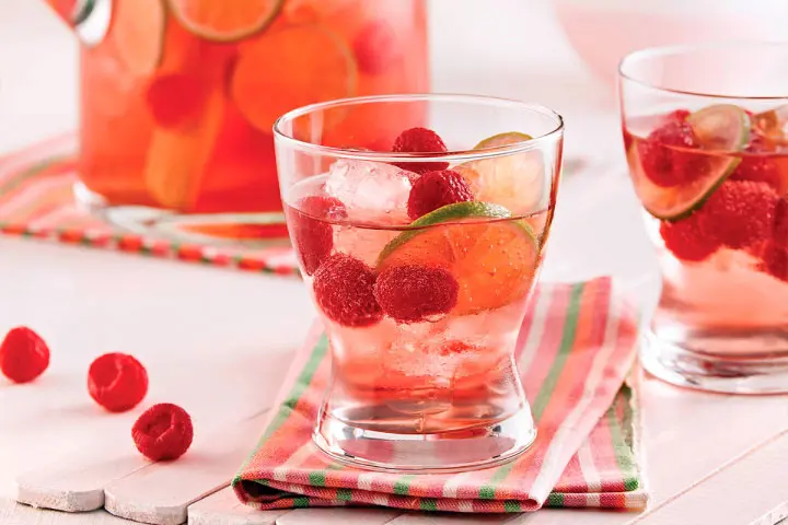 Punch made with rosé wine, white rum and lemon soda water with lime slices, raspberries and ice cubes