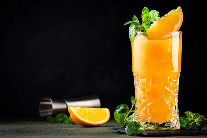 Mimosa made with sparkling apple cider and orange juice garnished with an orange wedge and mint