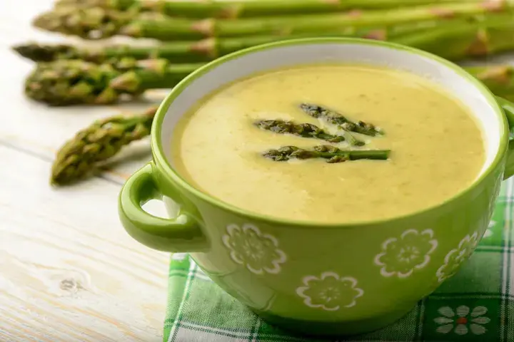 Recipe of leek cream with asparagus in a green bowl with green asparagus in the background